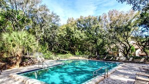 Uma piscina retangular com borda azulejada, cercada por um terraço de tijolos e espreguiçadeiras.