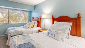 Quarto com duas camas, mesa de cabeceira com luminária e janela com persianas.