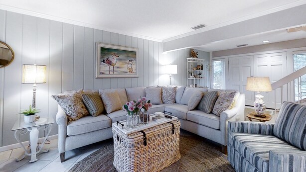 Sala de estar com sofá cinza, poltrona listrada e mesa de centro de vime com objetos decorativos.