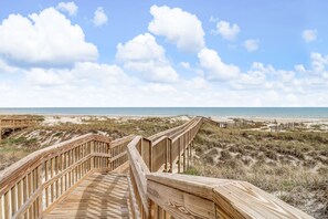 Pasarela de madera que conduce a una playa con dunas y cielo despejado.