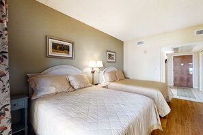 Une chambre d’hôtel avec deux lits, une table de chevet, une lampe et des tableaux encadrés au mur.