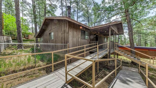 A cabin with a wooden exterior, a covered porch, and a wooden staircase leading to a deck. - Juniper Retreat (Ruidoso)