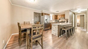 A modern kitchen with a central island, wooden dining table, and bar stools. - Juniper Retreat (Ruidoso)