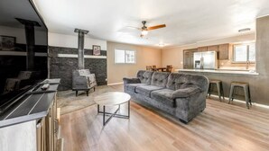 A modern living room with a fireplace, a sofa, a coffee table, and a kitchen area with a bar. - Juniper Retreat (Ruidoso)