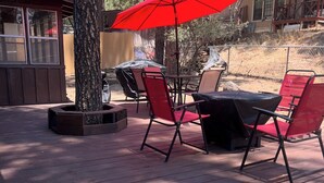 A deck with outdoor furniture, including a table and chairs, and a red umbrella. - Juniper Retreat (Ruidoso)