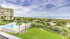 A resort with a swimming pool, lush greenery, and a view of the beach.