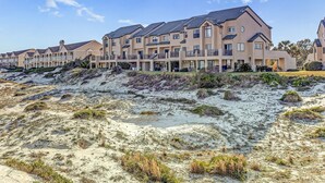 Een rij moderne, meerlaagse gebouwen met balkons, gelegen aan een zandstrand met schaarse begroeiing.