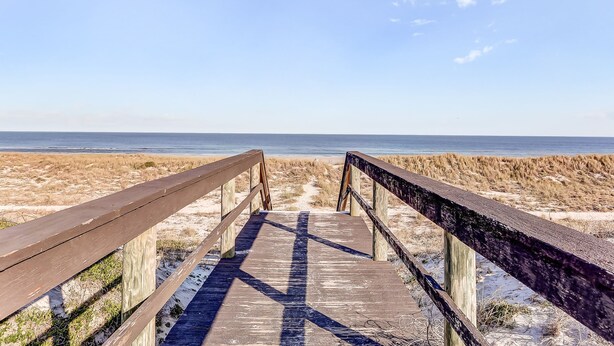 Une promenade en bois menant à une plage, avec un ciel dégagé.