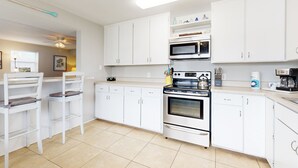 Una cocina moderna con armarios blancos, estufa, microondas y un comedor con dos sillas blancas.