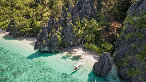 An aerial view of a tropical island with clear turquoise waters, rocky cliffs, and palm trees. - Modern Studio w/ Balcony • Smart Lock • Near Airport • Pool & WiFi • Netflix (Puerto Princesa City)