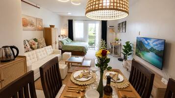 A well-lit dining area with a table set for a meal, a sofa, and a bed in the background.