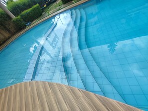 Une piscine à bord incurvé, avec une terrasse en bois en premier plan.