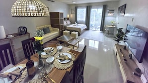 A modern living room with a dining area, a sofa, a bed, and a TV. - Modern Studio w/ Balcony • Smart Lock • Near Airport • Pool & WiFi • Netflix (Puerto Princesa City)