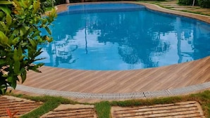 A swimming pool with a wooden deck, surrounded by lush greenery and a red-roofed building in the background. - Modern Studio w/ Balcony • Smart Lock • Near Airport • Pool & WiFi • Netflix (Puerto Princesa City)