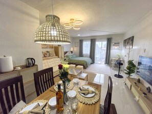 A modern living room with a dining area, a bed, and a TV. - Modern Studio w/ Balcony • Smart Lock • Near Airport • Pool & WiFi • Netflix (Puerto Princesa City)