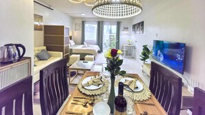 A modern living room with a dining area, a bed, a TV, and a large window. - Modern Studio w/ Balcony • Smart Lock • Near Airport • Pool & WiFi • Netflix (Puerto Princesa City)