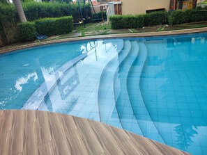 A swimming pool with a wooden deck in the foreground, surrounded by greenery and a building in the background. - Modern Studio w/ Balcony • Smart Lock • Near Airport • Pool & WiFi • Netflix (Puerto Princesa City)