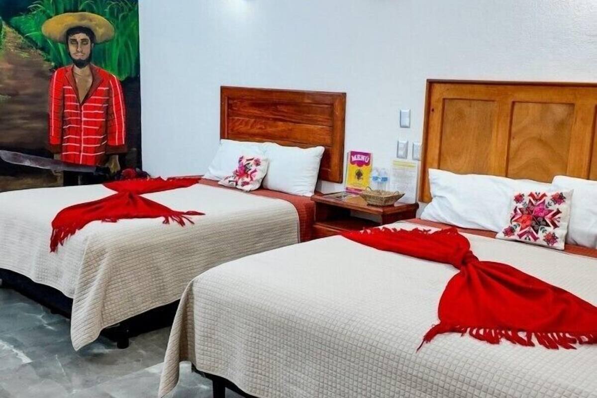 A hotel room with two beds, each with a wooden headboard and white bedding. There is a mural on the wall depicting a person in traditional attire.
