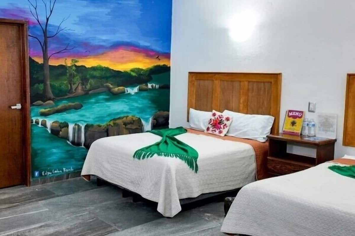 A hotel room with a bed, a nightstand, and a painting of a river scene on the wall.
