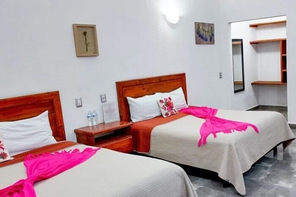 A hotel room with two beds, wooden headboards, white bedding, and a pink throw.