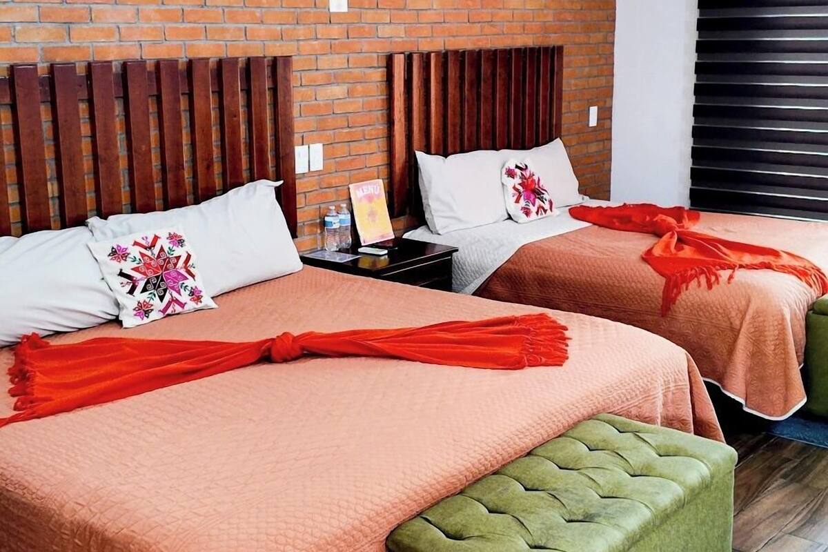 A hotel room with two beds, a brick wall, wooden headboards, and a blue rug.