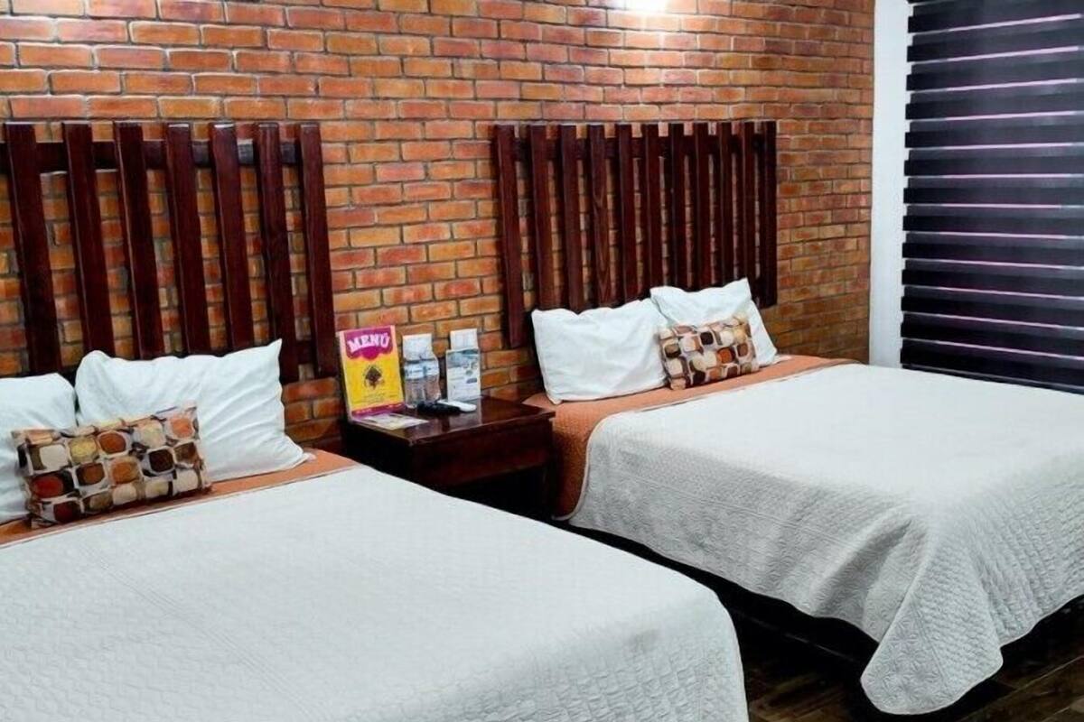 A hotel room with two beds, a brick wall, wooden headboards, and a window with blinds.