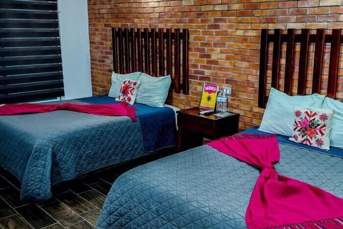 A hotel room with two beds, a brick wall, and a wooden headboard.