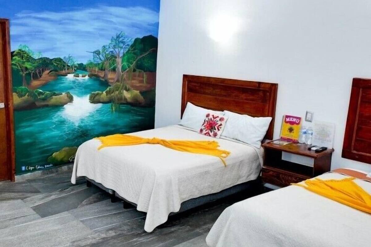 A hotel room with two beds, a mural of a river, and a wooden headboard.