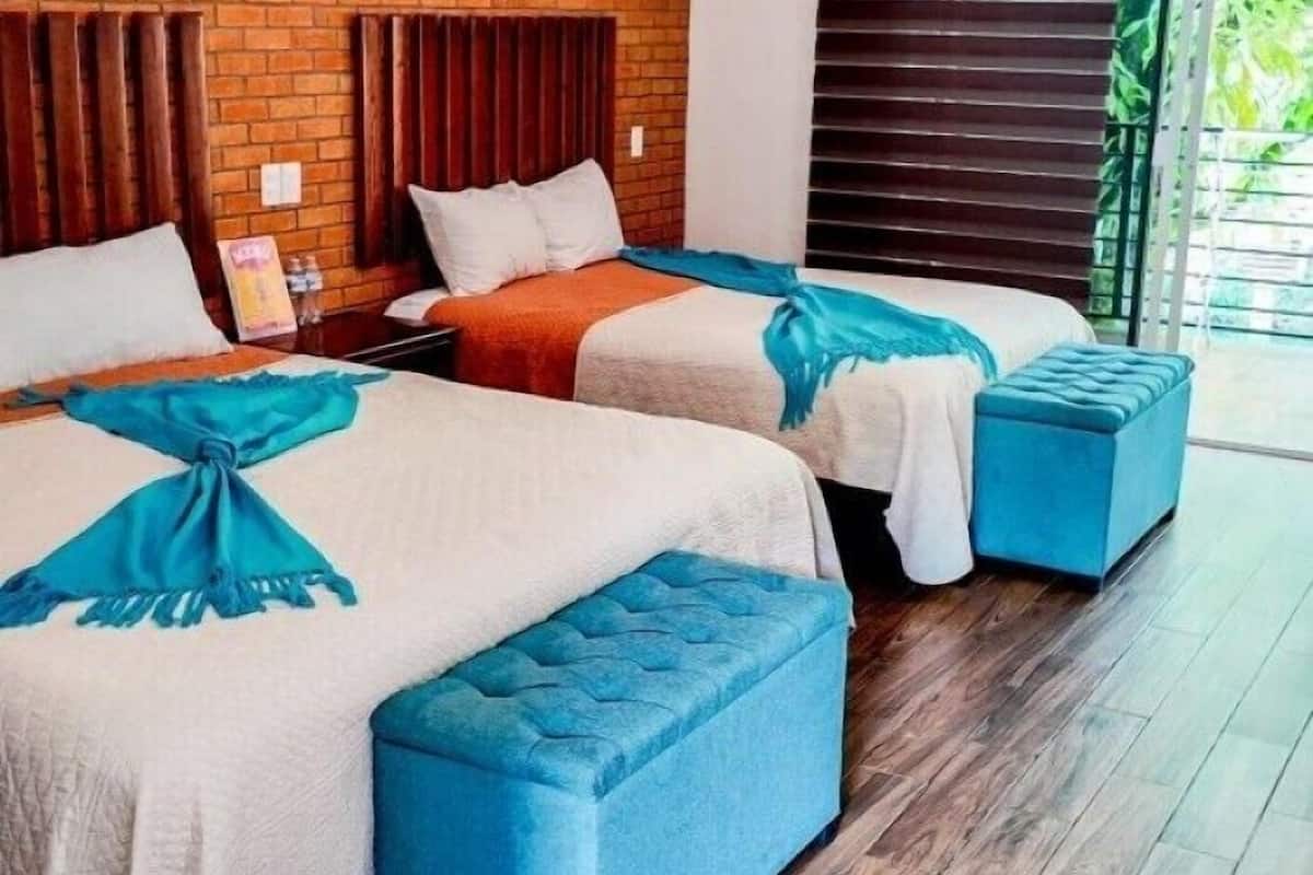 A hotel room with two beds, each with a blue headboard and matching ottoman, and a brick accent wall.
