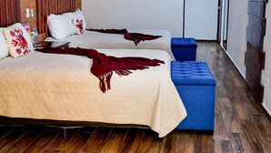 A hotel room with two beds, a brick accent wall, wooden flooring, and a mounted TV.