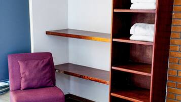 A room with a wooden floor, a purple armchair, a tall wooden bookshelf, and a brick wall.