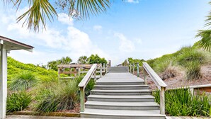 A wooden staircase leading to a covered area with a view of lush greenery and a clear sky. - Spacious condo with beach access, balcony, AC & outdoor pool (Fernandina Beach)