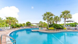 A swimming pool with a curved design, surrounded by palm trees and lounge chairs. - Spacious condo with beach access, balcony, AC & outdoor pool (Fernandina Beach)