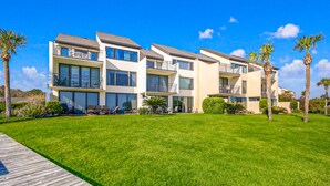 A modern multi-story residential building with balconies, a well-maintained lawn, and palm trees. - Spacious condo with beach access, balcony, AC & outdoor pool (Fernandina Beach)