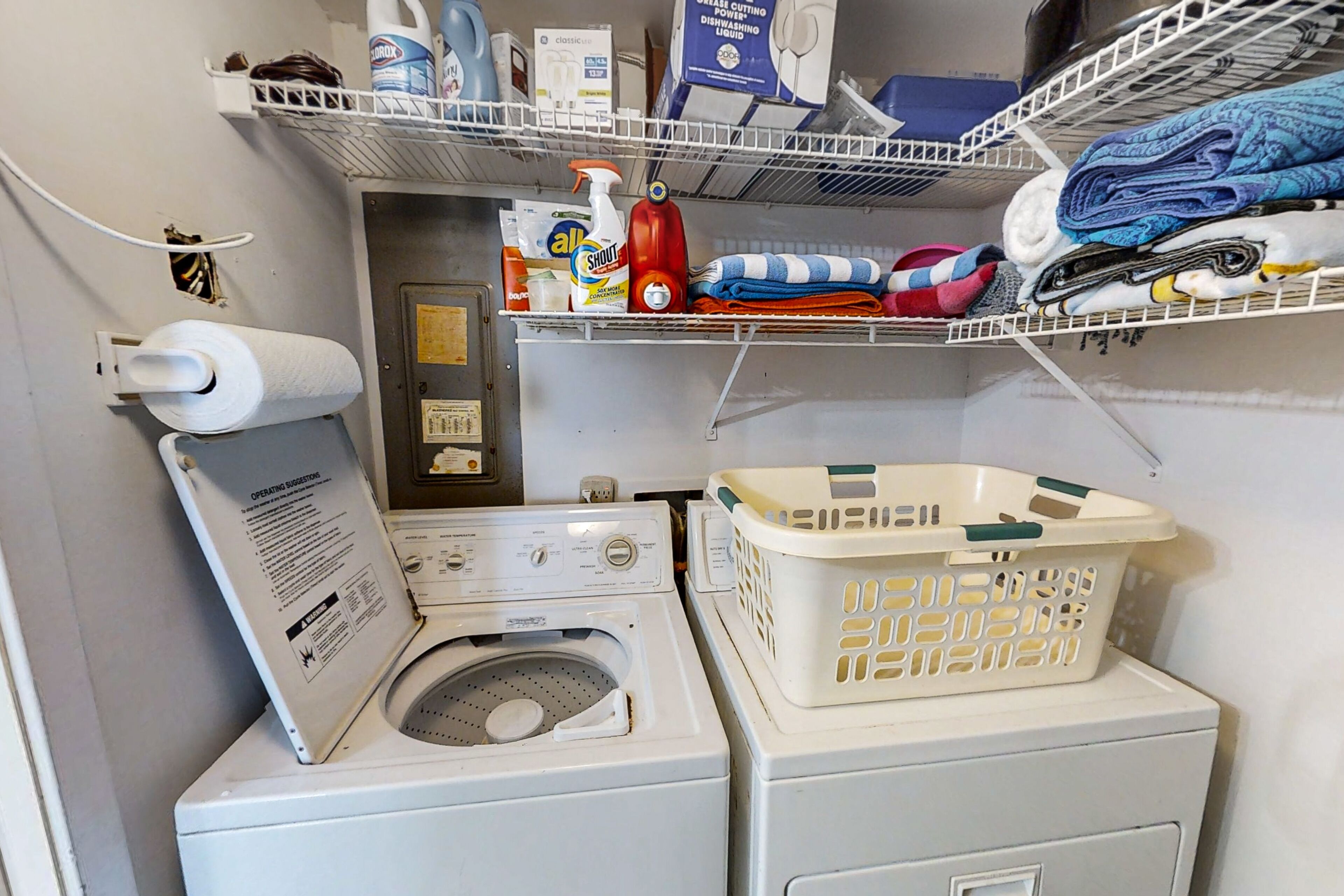 A laundry area with a washing machine, a dryer, and shelves with cleaning supplies and folded clothes.