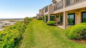 A row of modern two-story buildings with balconies, a well-maintained lawn, and a view of the beach.