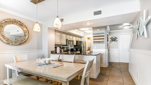 A modern kitchen with white cabinetry, a central island, and a dining area with a wooden table and chairs.