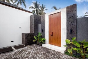 A modern building with a wooden door, concrete walls, and a brick floor. - Villa Ornella by BaliSuperHost (Bali)
