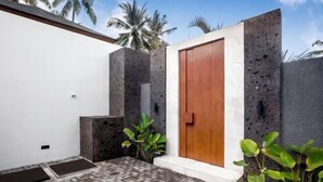 A modern building with a wooden door, a concrete wall, and a brick-paved area with plants. - Villa Ornella by BaliSuperHost (Bali)