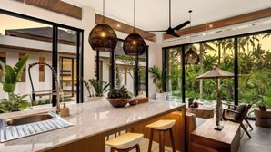 A modern kitchen with a large island, bar stools, and a view of lush greenery outside. - Villa Ornella by BaliSuperHost (Bali)