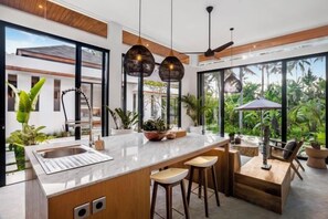 A modern kitchen with a large island, bar stools, and a view of the outdoors. - Villa Ornella by BaliSuperHost (Bali)