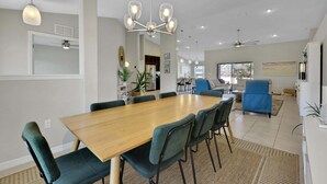 Un espace de salle à manger moderne avec une table en bois et des chaises recouvertes d’un tissu vert, un lustre et un ventilateur de plafond.