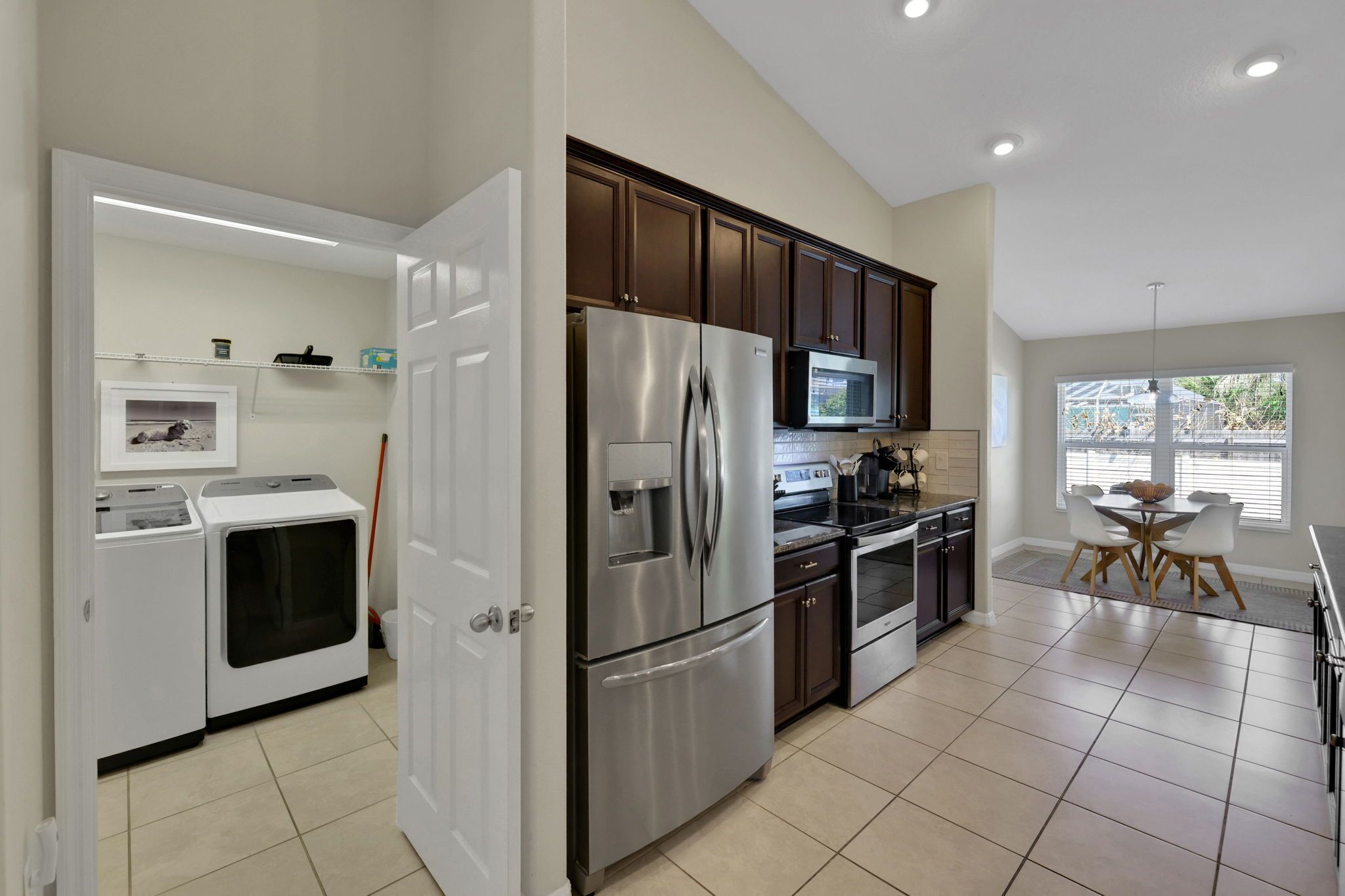 A modern kitchen with stainless steel appliances, a dining area with a table and chairs, and a laundry room.