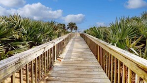 A wooden boardwalk leading to a beach with palm trees on both sides. - Elegant waterfront condo with central AC, balcony, and shared pools & hot tubs (Palm Coast)