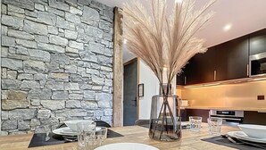 Un área de comedor moderna con una pared de piedra, una mesa de madera con platos y cubiertos blancos, y un jarrón decorativo con plumas de pámpano.