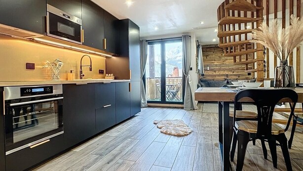 Una cocina moderna con armarios oscuros, hornos empotrados y una mesa de comedor de madera con sillas.