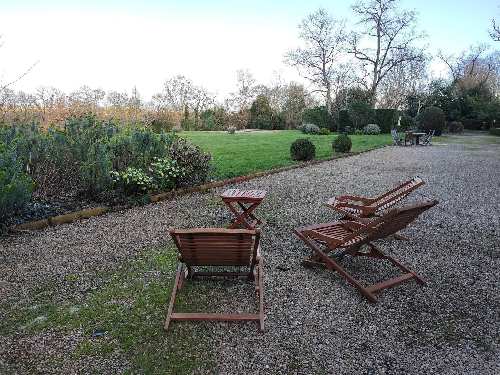 A gravel patio with two wooden lounge chairs and a small table.