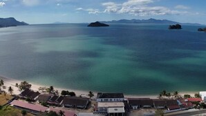 A coastal view with clear turquoise waters, a sandy beach, and several buildings with red roofs. - Nazrat Residence (Langkawi)
