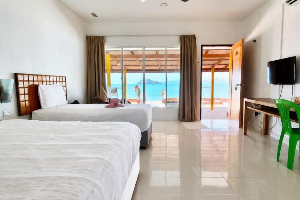 A hotel room with two beds, a TV, a desk, and a view of the beach.