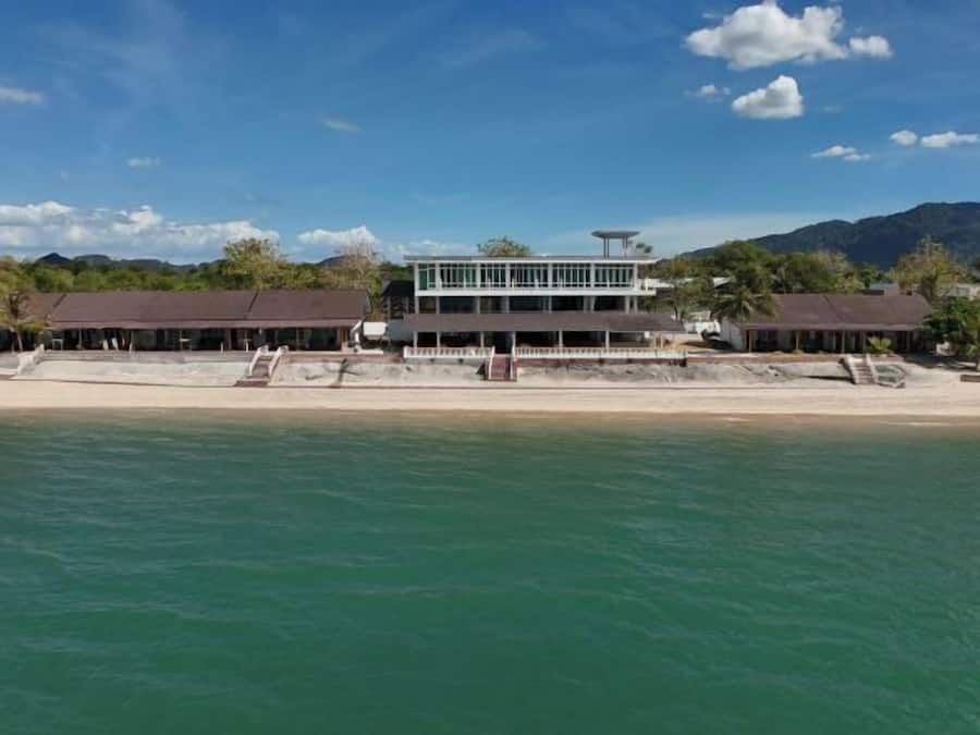A beachfront hotel with a two-story structure, a pool, and a beach in the foreground.